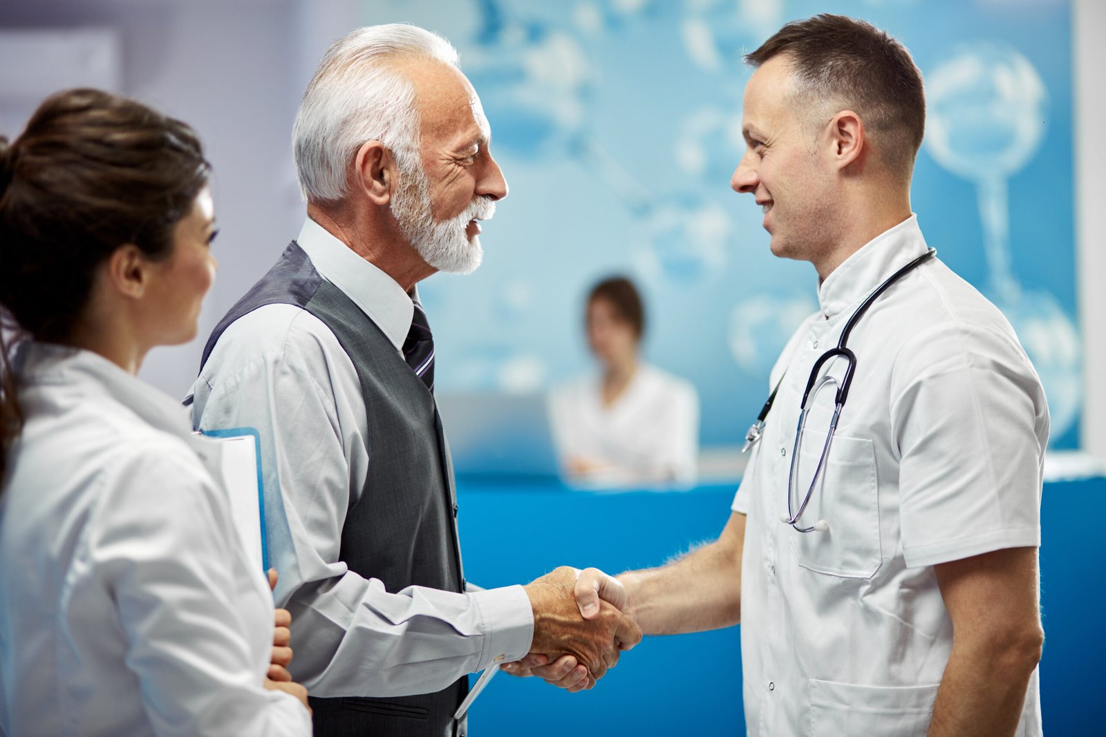 Happy senior businessman and doctor shaking hands while greeting in a hallway at the hospital.